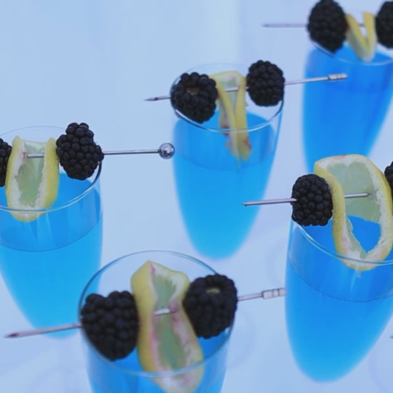 blue cocktail garnished with lemon and blueberries in glass
