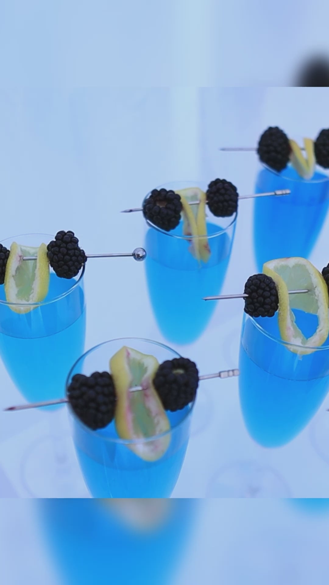 blue cocktail garnished with lemon and blueberries in glass