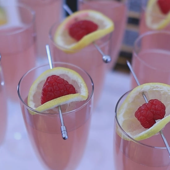 pink cocktail in glass garnished with lemon and raspberry