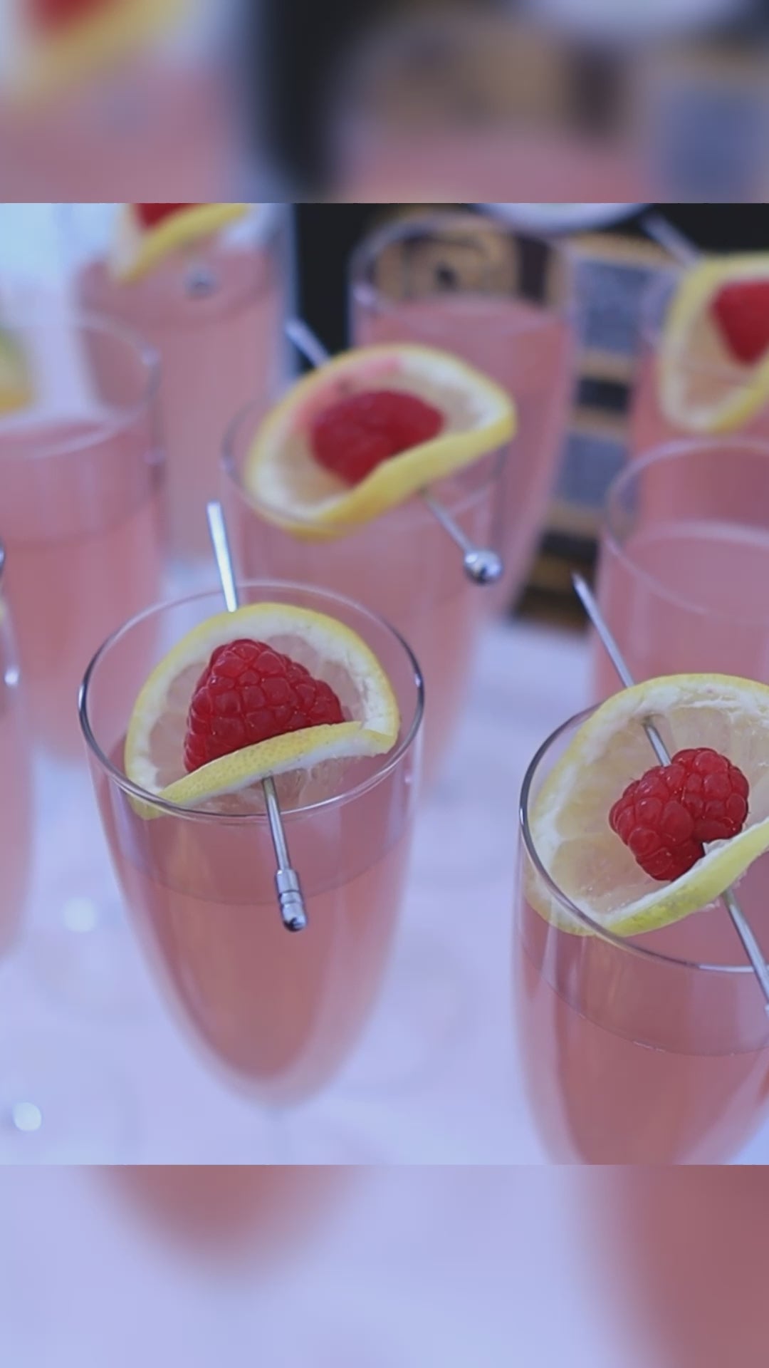 pink cocktail in glass garnished with lemon and raspberry