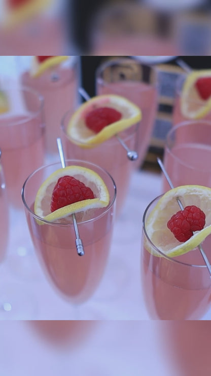 pink cocktail in glass garnished with lemon and raspberry